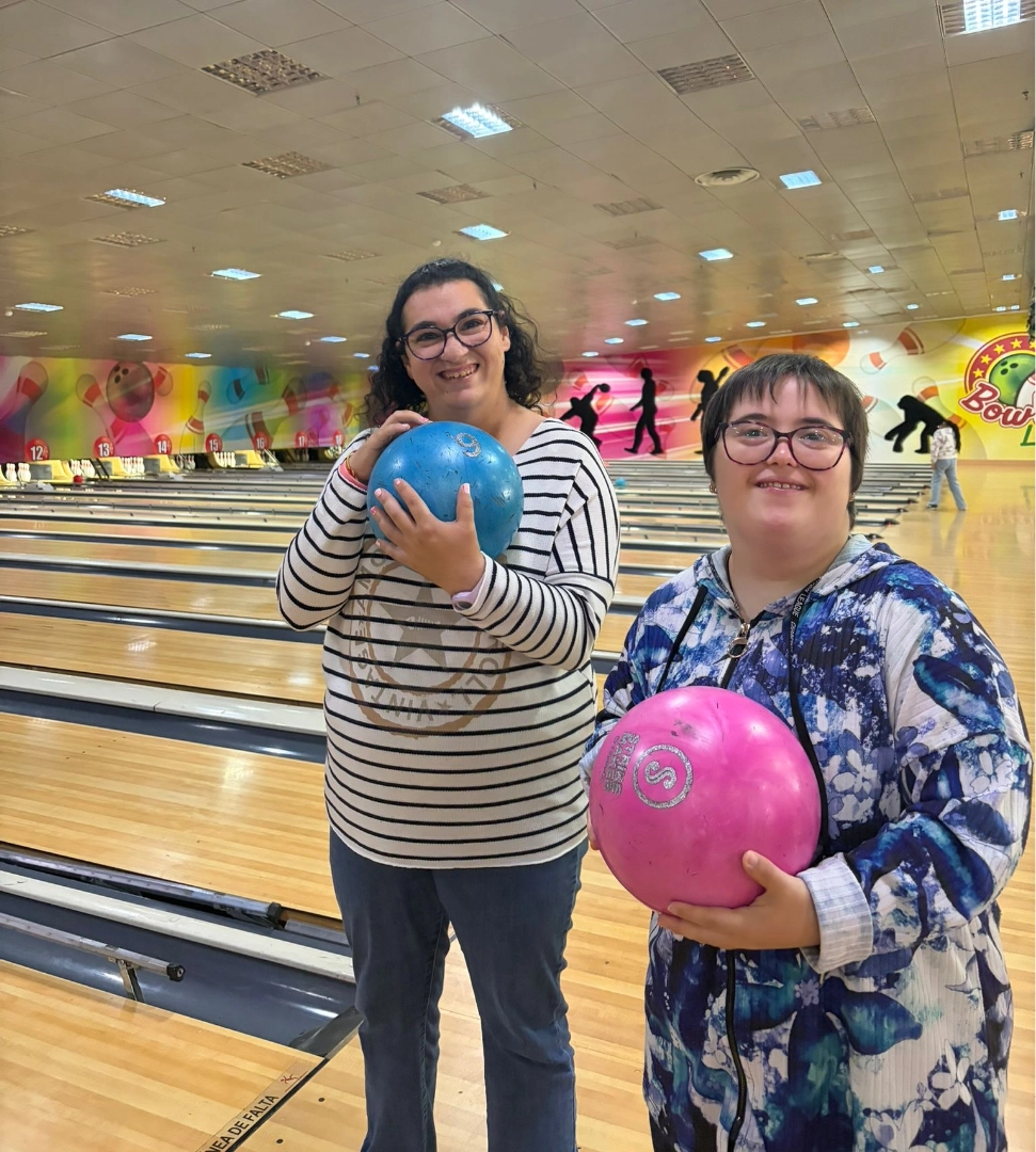 Dos personas usuarias participan en una actividad de ocio en una bolera.